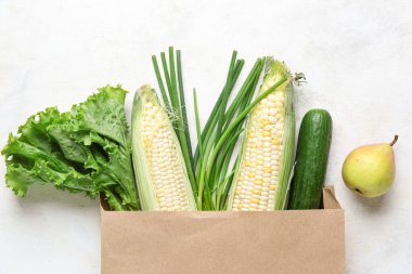 Beyaz arka planda yeşillik, armut ve sebzeli kağıt torba.