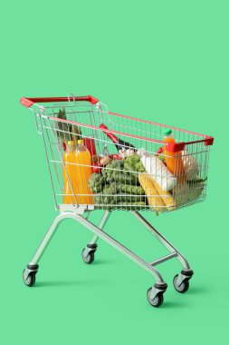 Yeşil arka planda farklı yiyeceklerle dolu alışveriş arabası.
