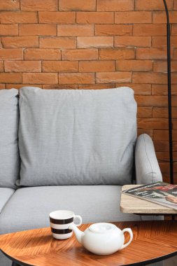 Kahverengi tuğla duvarın yanındaki rahat gri kanepeli modern oturma odasının içinde.