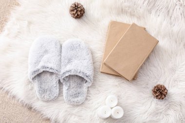 Yumuşak terlikler, mum ve kürk halısı üzerine kitaplar.