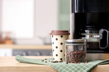 Modern kahve makinesi, fasulye ve kağıt bardak mutfaktaki ahşap masada.