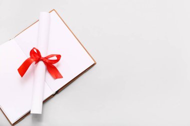 Kırmızı kurdeleli diploma ve beyaz arkaplan üzerine açık kitap