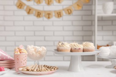 Beyaz tuğla duvara karşı doğum günü partisi için farklı şekerlerle dolu bir masa.