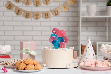 Beyaz tuğla duvara karşı doğum günü partisi için pasta, şeker ve dekor.