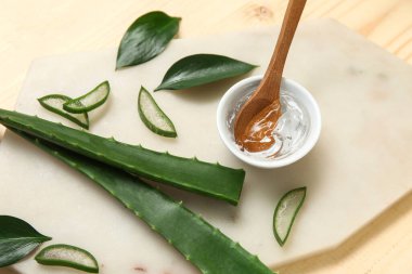Ahşap arka planda yaprakları olan bir kase aloe vera jel ve pansiyon.