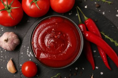 Bir kase taze domates sosu ve siyah arka planda sarımsak.