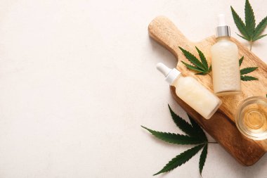 Şişeler ve cam kase beyaz arka planda yaprakları olan kenevir kozmetik yağı.