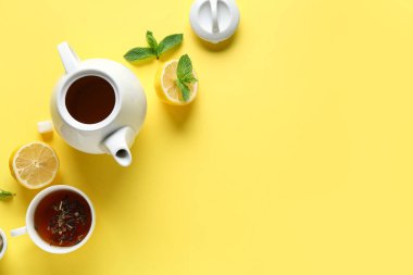 Şık çay demliği, bir fincan çay, sarı arka planda limon ve yeşil yapraklar.