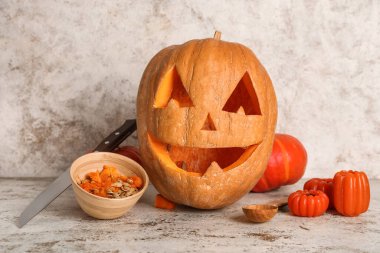 Ahşap bir kase tohumla oyulmuş Cadılar Bayramı kabağı, beyaz grunge arka planda kaşık ve mumlar