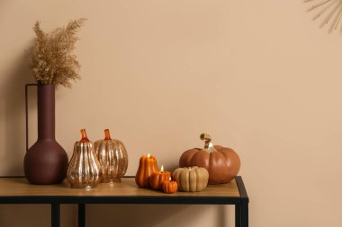 Evdeki bej duvarın yanındaki masada vazo ile balkabağı şeklinde mumlar yakıyor.