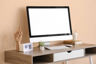 Ofisteki bej duvarın yanında modern bilgisayar, saat ve kırtasiye ile şık bir iş yeri