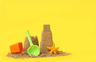 Sarı arka planda deniz yıldızı ve plaj oyuncakları olan güzel bir kumdan kale.