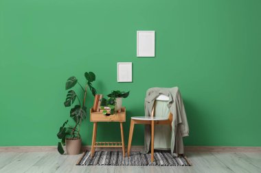 Modern odanın içindeki yeşil duvarın yanındaki sandalye, masa ve bitkiler.
