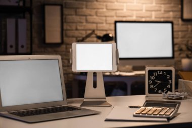 Blank laptop with tablet computer on desk in office at night