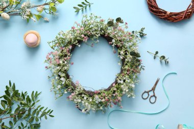 Composition with Easter wreath, green twigs, flowers and egg on blue background