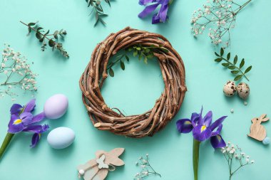 Composition with Easter wreath, flowers, green twigs and eggs on turquoise background