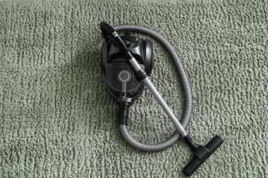 Yeşil halıda modern elektrikli süpürge, üst manzara.