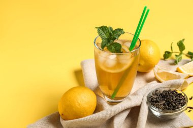 Sarı arka planda naneli ve kuru yapraklı limonlu buzlu çay, yakın plan.