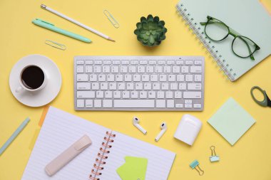 Klavyeli kompozisyon, bir fincan kahve ve sarı arka planda farklı kırtasiye malzemeleri.