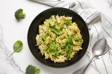 Beyaz arka planda brokoli ve fesleğen yapraklı siyah fusilli makarna kasesi.