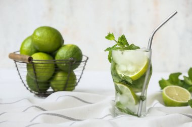 Bir bardak taze mojito kokteyli ve beyaz arka planda nane ve limon sepeti.