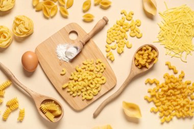 Farklı türde ham makarna, ahşap kesim tahtası ve bej arkaplanlı yumurta kompozisyonu