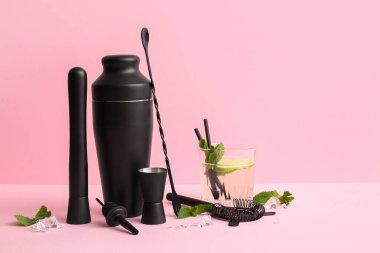 Farklı barmen aletleri ve pembe arka planda bir bardak lezzetli kokteyl.