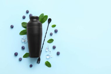 Titretici, karıştırma kaşığı, yabanmersini, nane yaprağı ve mavi arkaplanda buz küpleriyle kompozisyon