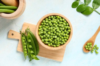 Ahşap kesme tahtası ve kase mavi grunge arka planda taze bezelyeler, yakın plan.