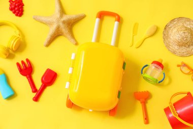 Çocuk bavulu, oyuncaklar ve plaj aksesuarları sarı arka planda, yakın plan