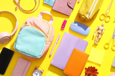 Sarı arka planda modern cep telefonu ve okul malzemelerine sahip kompozisyon