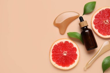 Kozmetik ürün şişesi, yüz masajı aletleri ve bej arka planda bir dilim greyfurt, yakın plan.