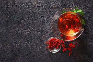 Bir bardak sıcak goji çayı ve arkaplanda da nane ve böğürtlen.