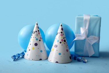 Parti şapkalı doğum günü kompozisyonu, hediye kutusu ve mavi arka planda balonlar, yakın plan.
