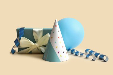 Parti şapkası, hediye kutusu ve balonla bej arka planda doğum günü kompozisyonu, yakın plan