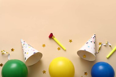 Parti şapkaları, balonlar, ıslıklar ve bej arka planda konfetileri olan doğum günü kompozisyonu