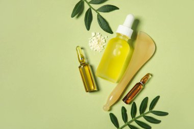 Yüz masajı aracı, yapraklar, bir şişe kozmetik ürünü ve yeşil arka planda kolajen tozu, yakın plan.