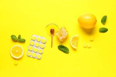 Ballı boğaz pastilleri, nane yaprakları ve sarı arka planda limon.