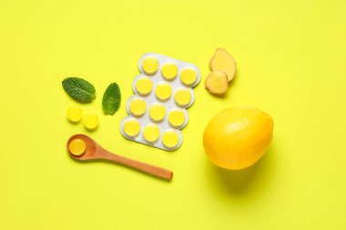 Gırtlak pastilleri, zencefil kökü, nane yaprakları ve sarı arka planda limon.