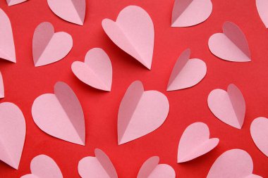 Kırmızı zemin üzerinde pembe kağıt kalpler olan kompozisyon, yakın plan. Sevgililer Günü kutlaması