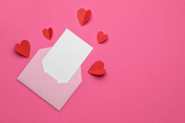 İçinde boş kart ve pembe arka planda kırmızı kağıt kalpler olan bir zarf. Sevgililer Günü kutlaması