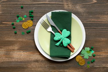 Kahverengi ahşap arka planda madeni paralar ve dekoratif yoncalarla Aziz Patrick Günü kutlamaları için masa ayarlayın.