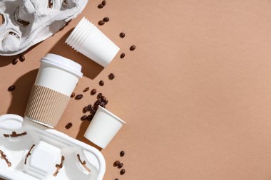 Kahverengi arka planda kağıt bardaklar, kahve çekirdekleri ve tutacakları olan kompozisyon