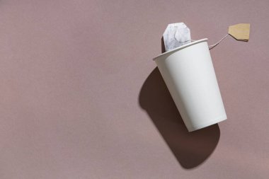 Kahverengi arka planda çay poşeti olan kağıt bardak, yakın plan.