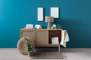 Mavi duvarın yanında temiz havlular ve lamba olan çekmeceler.