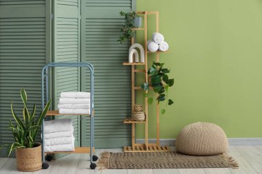 Odanın içinde raflar, temiz havlular ve katlanır ekran var.