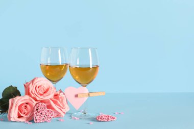 Gül çiçekli şarap kadehleri ve mavi arka planda dekoratif kalpler. Sevgililer Günü kutlaması