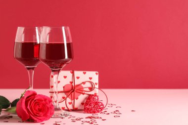 Gül çiçekli şarap kadehleri, hediye kutusu ve renk arkaplanlı dekoratif kalp. Sevgililer Günü kutlaması