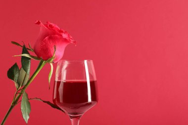 Kırmızı arka planda gül çiçekli bir bardak şarap. Sevgililer Günü kutlaması
