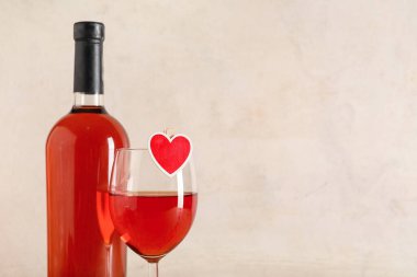 Cam kaplı bir şişe şarap ve hafif arka planda dekoratif kalp. Sevgililer Günü kutlaması